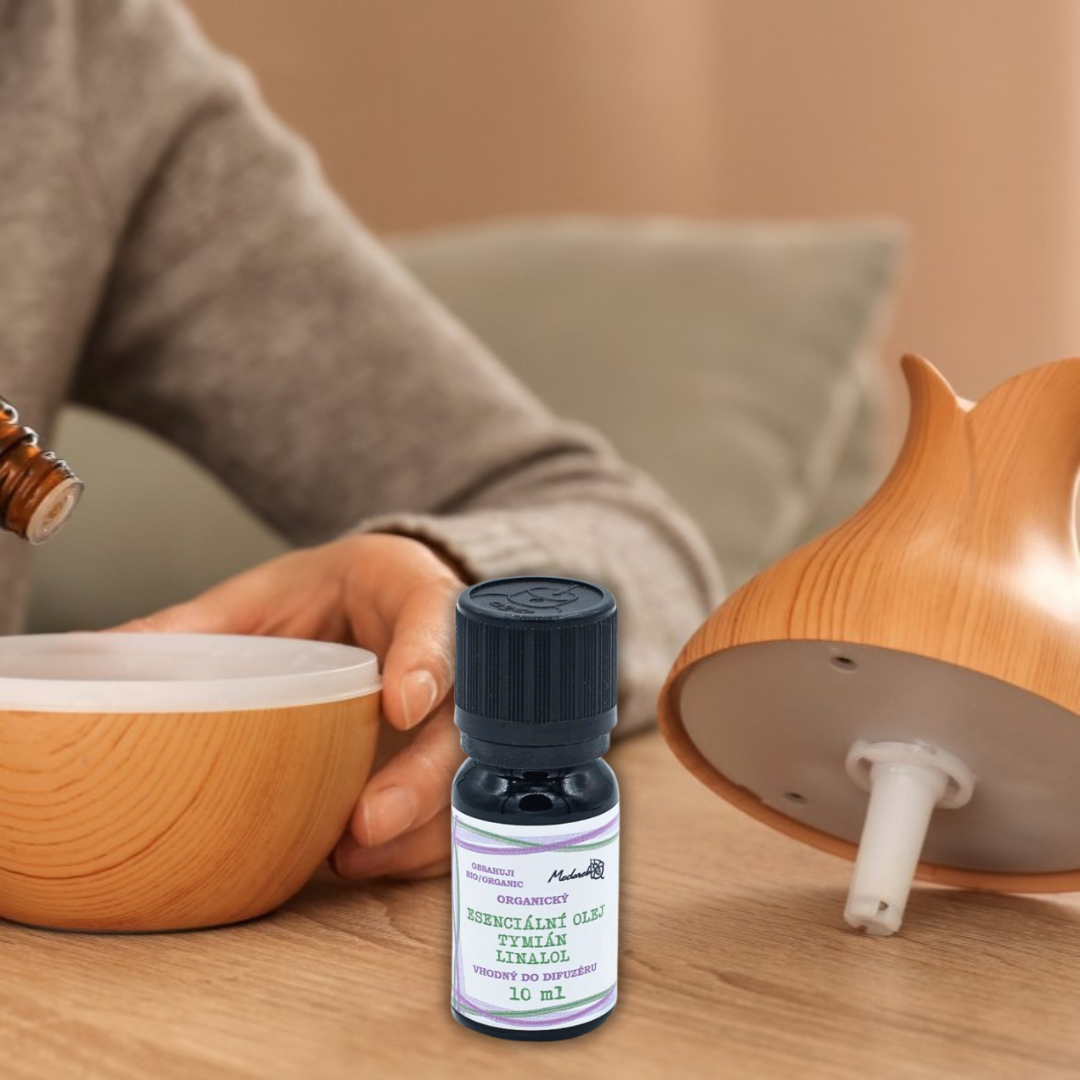 Thyme diffuser essential oil (Tymian Linalool) 10 ml bottle from Medarek in front of a wooden ultrasonic diffuser while a person adds drops.